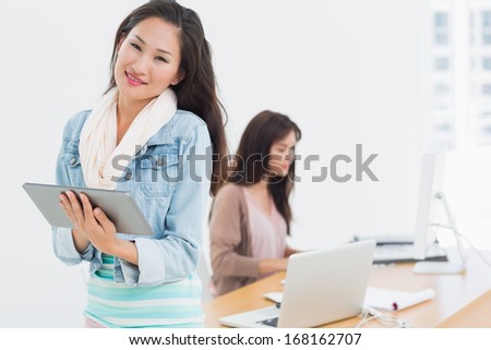 Portrait of a casual female artist using digital tablet with colleague in the background at a bright office