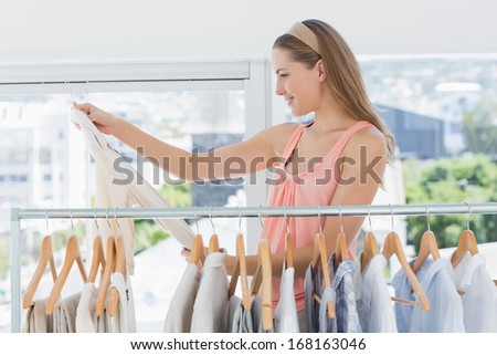 Beautiful female fashion designer looking at shirt beside rack of clothes in the store