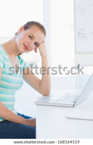 Portrait of a smiling young casual woman in front of laptop at a bright office