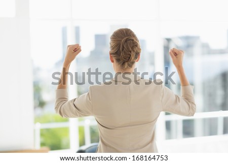 Rear of a cheerful young businesswoman clenching fists in a bright office