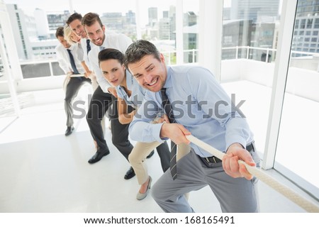Full length of a group of business people pulling rope in a bright office