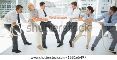 Full length of a group of business people playing tug of war in office
