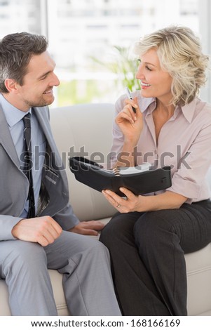 Smart businessman and his secretary with diary sitting on sofa at home