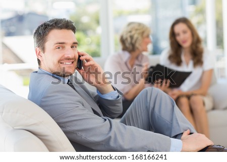 Businessman on call with female colleagues sitting on sofa in background at home