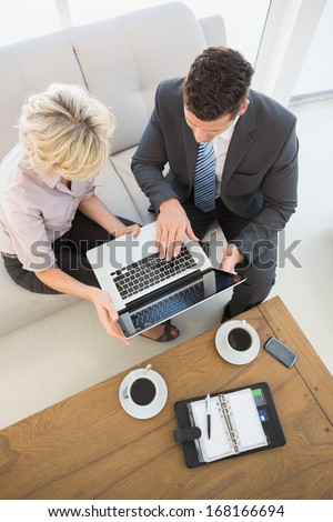 High angle view of a businessman and his secretary with laptop and diary sitting on sofa at home