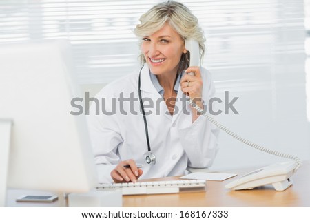 Portrait of a smiling female doctor with computer using phone at medical office