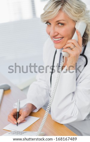 Side view of a female doctor using phone while writing notes at medical office