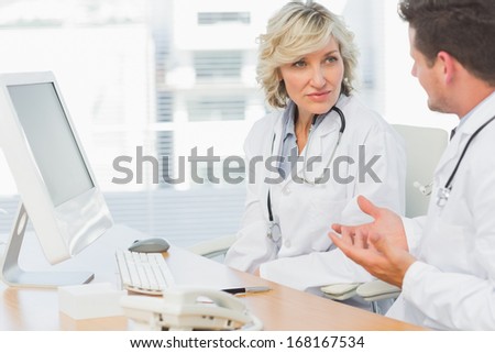 Two concentrated doctors discussing something by computer at medical office