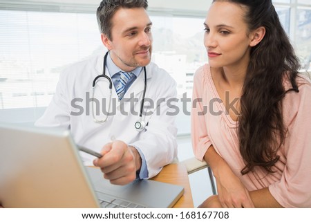 Male doctor showing something on laptop to patient at desk in medical office