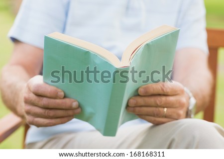 Close-up mid section of a relaxed senior man reading a book at the park