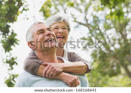 Cheerful senior woman embracing man from behind at the park