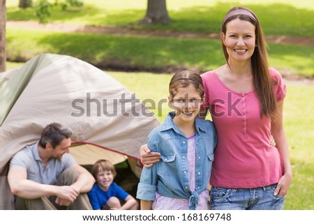 Portrait of mother and daughter with family behind in the park