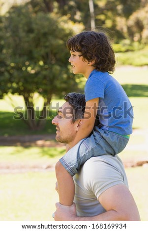 Side view of a smiling man carrying son on his shoulders in the park