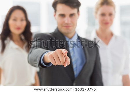 Smiling businessman pointing to camera in front of his team in the office