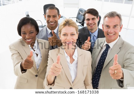 Diverse close business team smiling up at camera giving thumbs up in the office