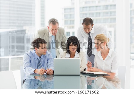 Business people gathered around laptop talking in the office