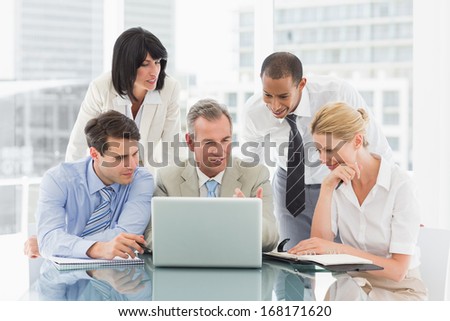 Happy business people gathered around laptop looking at it in the office