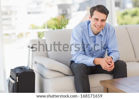 Smiling businessman sitting on couch waiting to leave on business trip in the office