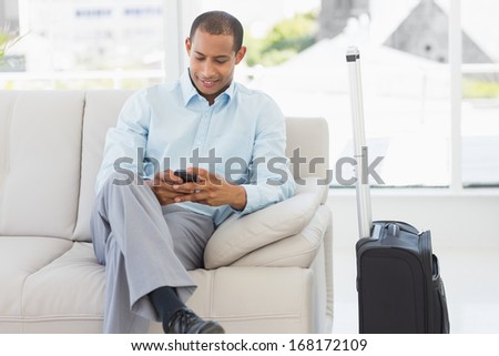 Man sitting on sofa sending a text waiting to depart on business trip in the office