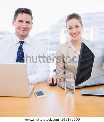 Smartly dressed young man and woman using computer and laptop at office desk