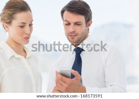 Smartly dressed young man and woman looking at mobile phone in a bright office
