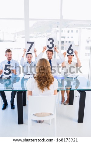 Group of panel judges holding score signs in front of a woman at bright office