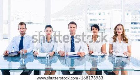 Portrait of smartly dressed young executives sitting in row at desk in a bright office