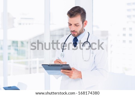 Concentrated male doctor writing reports in clipboard at the hospital