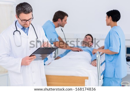 Doctor writing reports with patient and surgeons in background at the hospital
