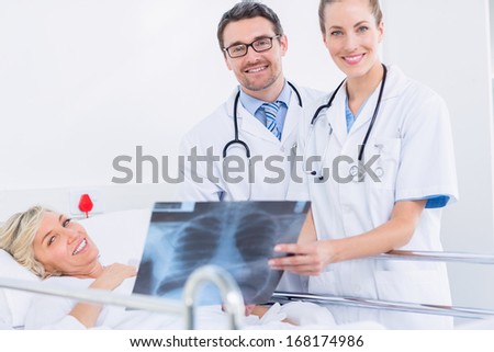 Portrait of smiling doctors showing x-ray to female patient in bed at the hospital