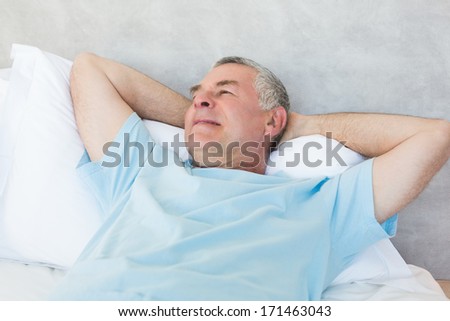 Senior man with hands behind head day dreaming in bed