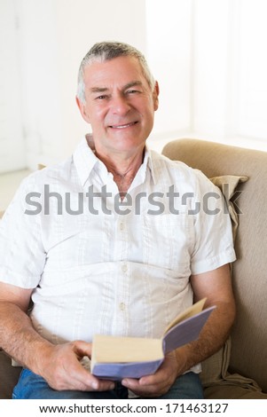 Portrait of smiling senior man holding book on sofa at home