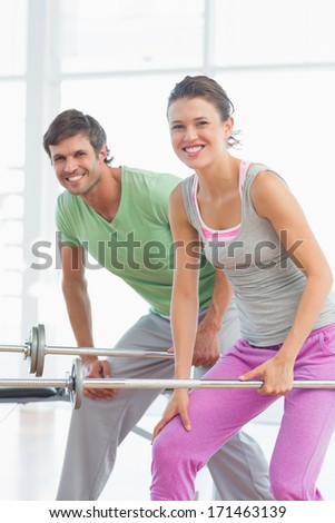 Portrait of a fit young man and woman lifting barbells in the gym
