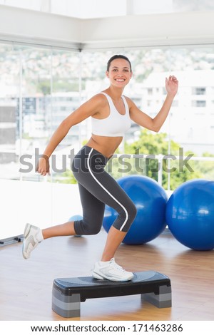 Full length side view of a fit young woman performing step aerobics exercise in gym