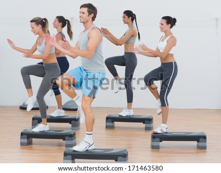 Full length side view of fitness class performing step aerobics exercise in gym