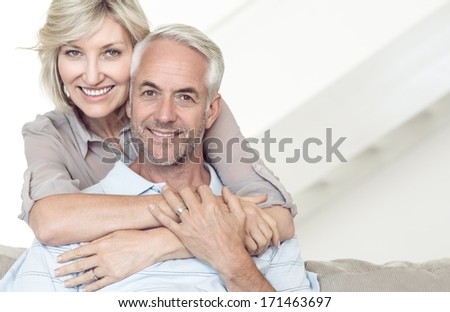 Portrait of a smiling woman embracing mature man from behind on sofa at home
