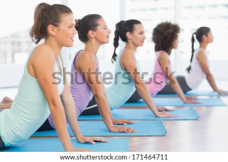 Side view of a fit class doing the cobra pose in a bright fitness studio