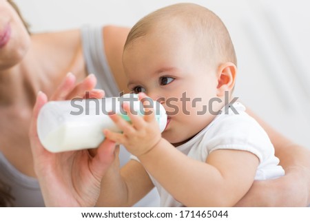 Close-up of mother feeding baby with milk bottle in bed at home