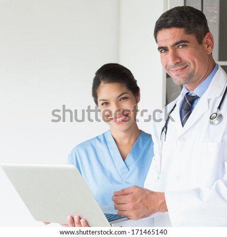 Portrait of confident doctor and female nurse using laptop in hospital