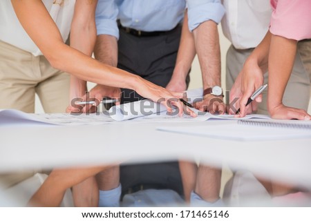 Mid section of business people studying blueprint at desk in office