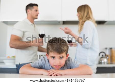 Portrait of sad boy leaning on table while parents arguing in background at home
