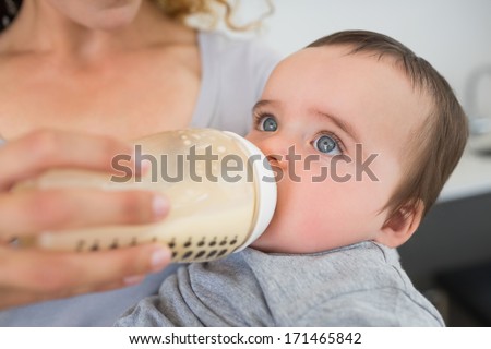 Mother feeding milk to baby boy from bottle at home