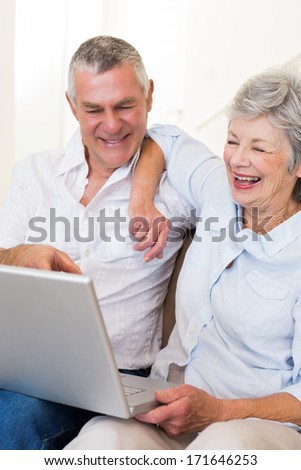 Happy senior couple looking at laptop while sitting on sofa at home