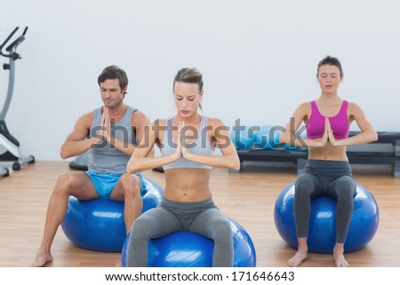 Sporty young people with joined hands sitting on exercise balls in the gym