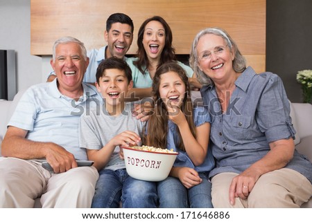 Portrait of happy extended family watching tv on sofa in the living room at home