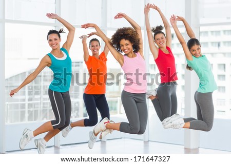 Full length portrait of fitness class and instructor jumping in fitness studio