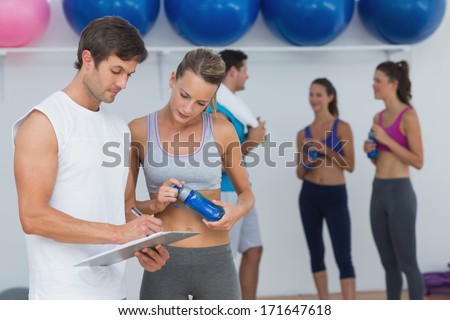 Couple looking at clipboard with fitness class in background at the gym