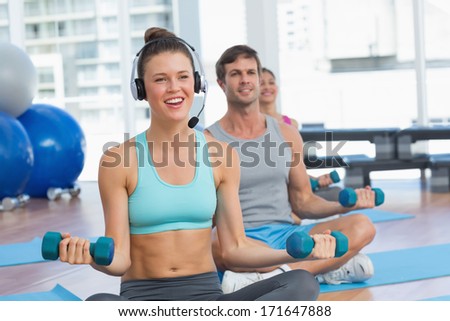 Smiling fit people listening to music while lifting dumbbell weights in a bright gym