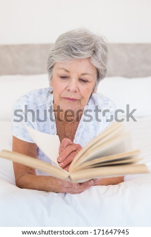 Concentrated senior woman reading story book in bed