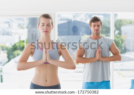 Young sporty couple with joined hands and eyes closed in fitness studio